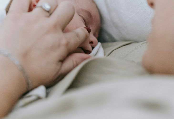 Adult lay alongside sleeping baby, gently stroking babies face