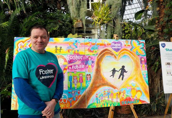 Foster carer Phil stood in front of fostering artwork in Sefton Park, Palm House