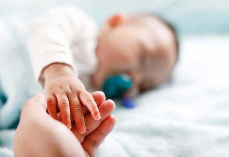 Baby sleeping and holding adults hand