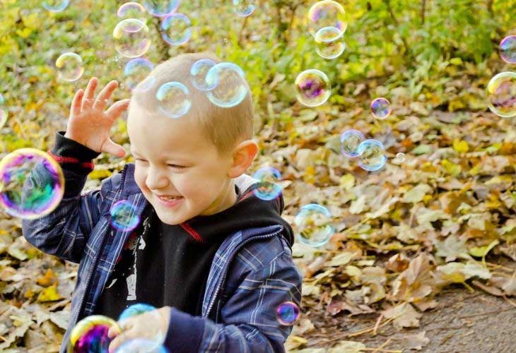 Young boy smiling as he pops bubbles at the park